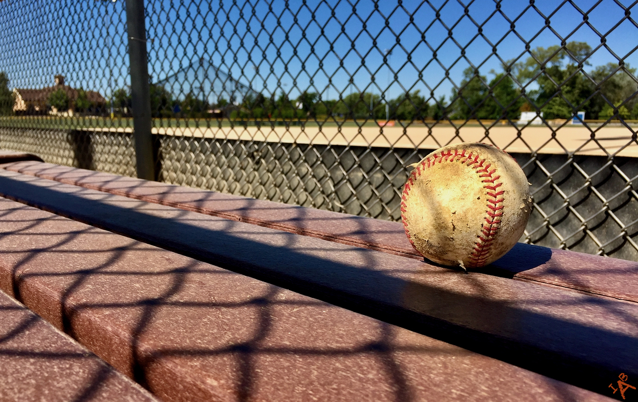 Picture of a baseball on a bench at a baseball diamond.