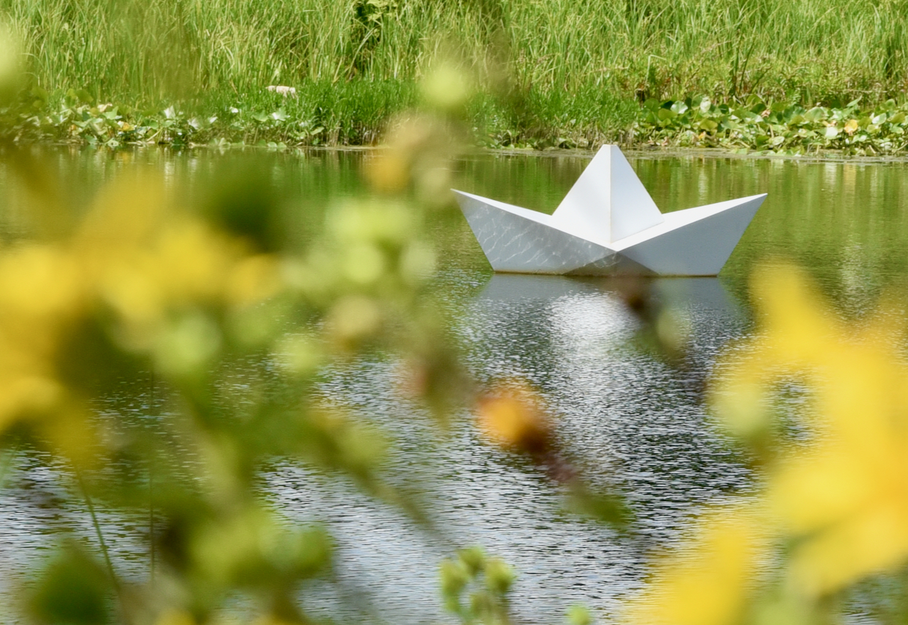 A piece of art that looks like a paper boat origami floats in the water.