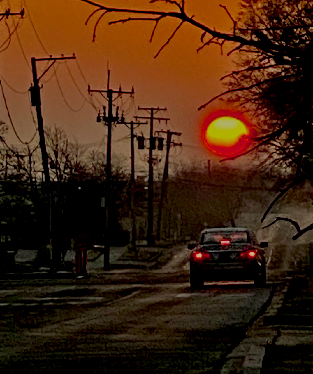 Car driving down a road to a rising sun.