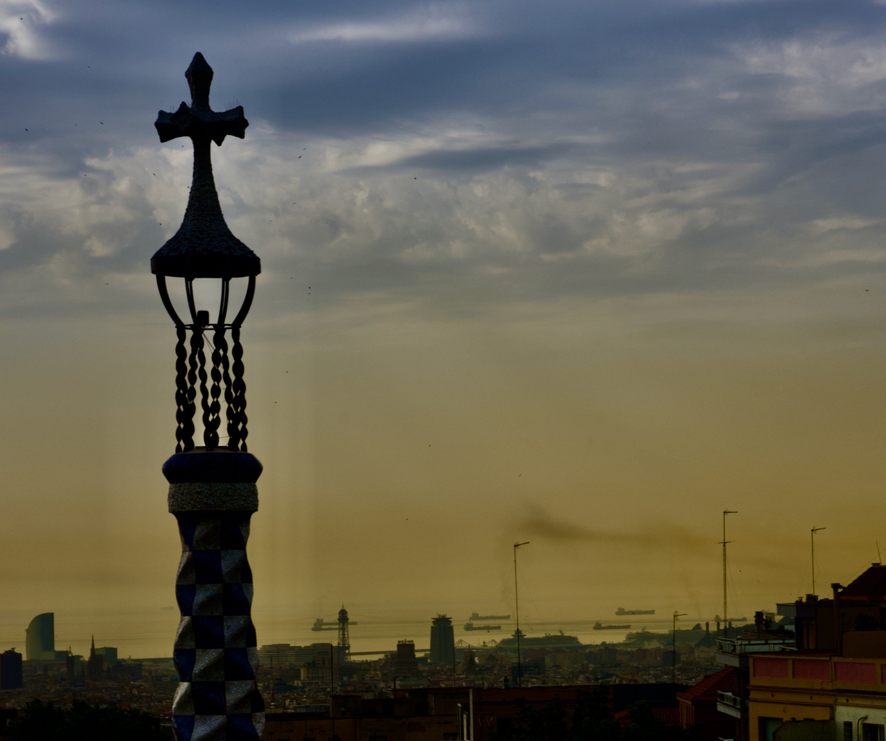Shipping boats line up outside of Barcelona while a cross rises above the city.