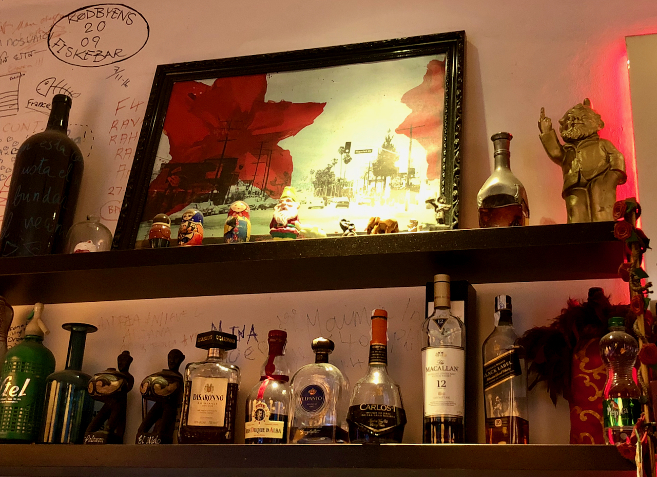 A stock of liquor at a bar with a gnome flipping the middle finger.